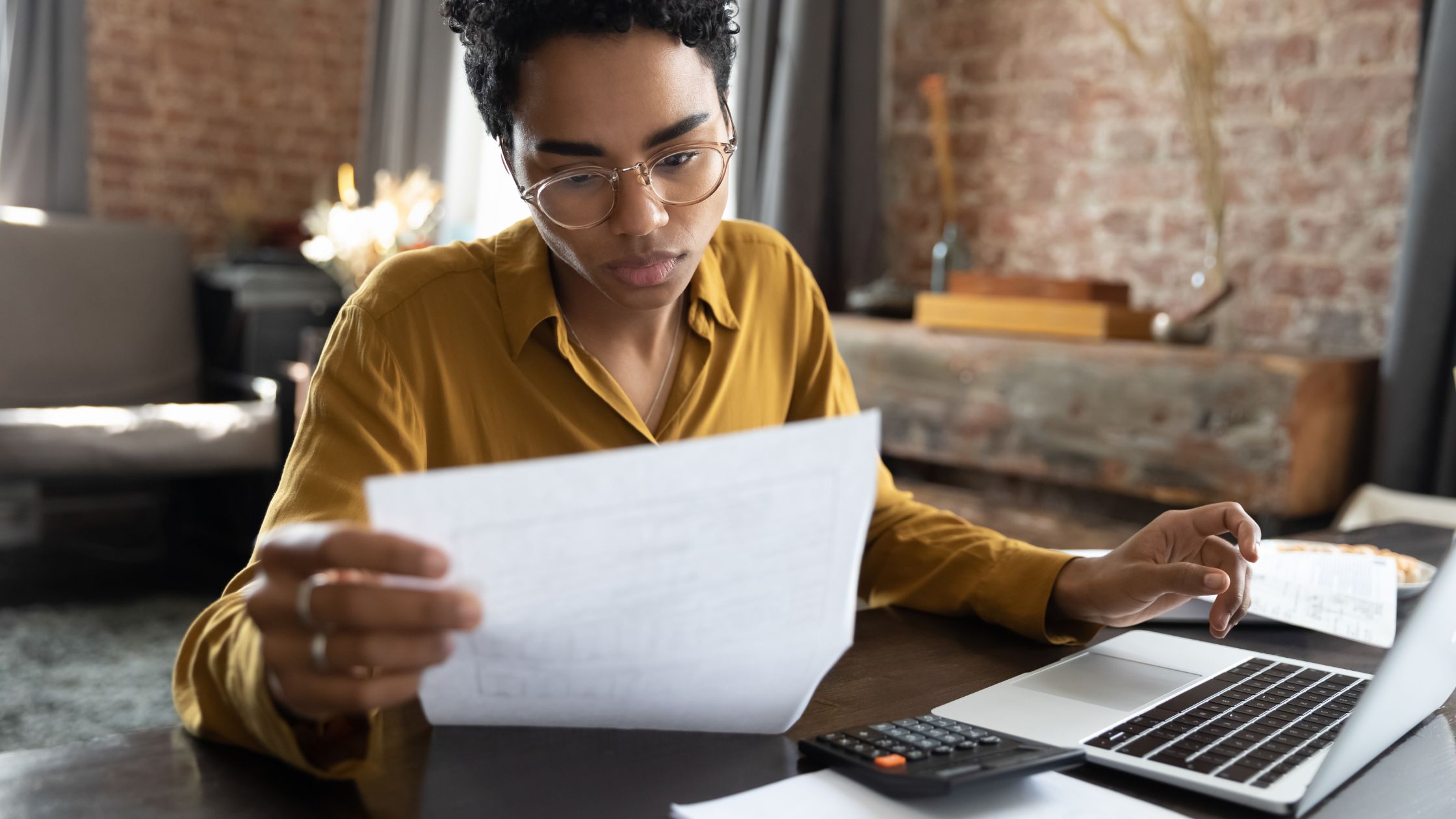 Focused woman reviewing tax documents with a laptop and calculator, representing non-resident tax filing support in Canada.