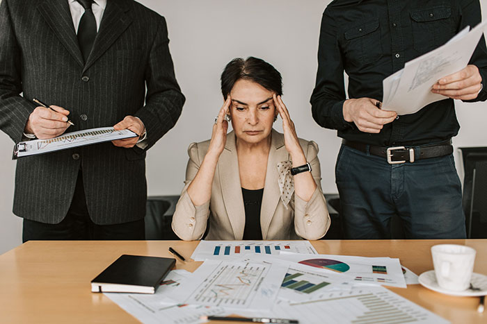 A business owner holds her head while looking at a desk full of paperwork