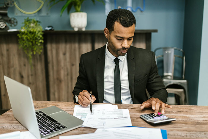 A man in a suit sitting at a desk with a laptop and calculator