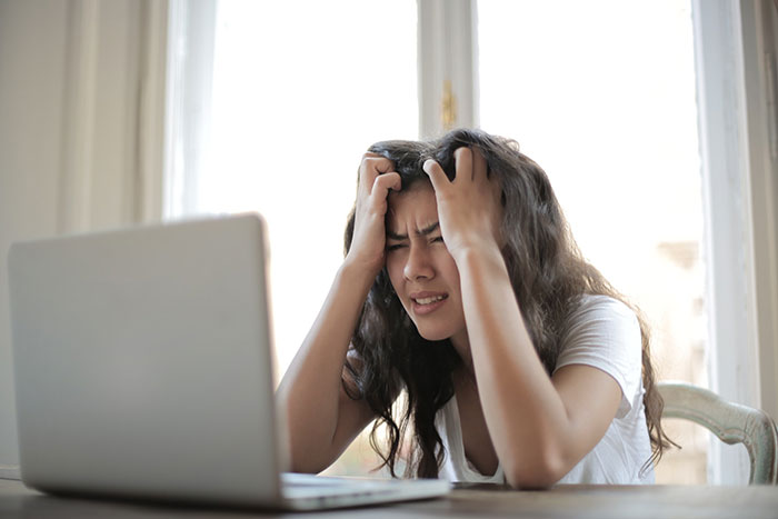 A stressed-out woman holds her head while looking at her laptop.