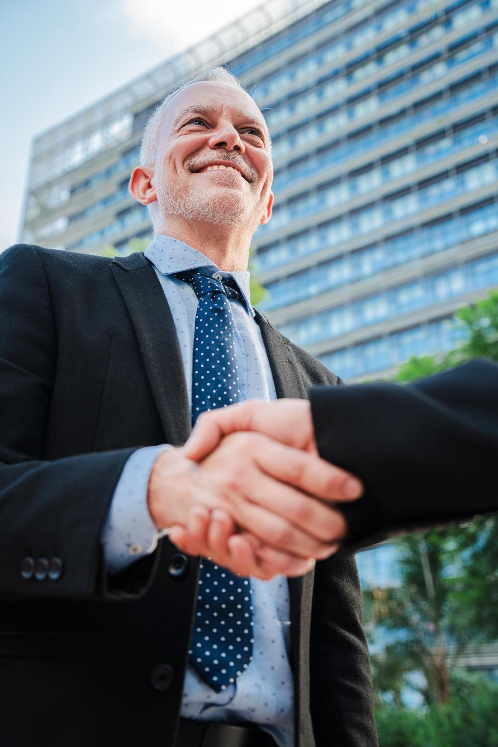 Vertical portrait of a person in a suit smiling and shaking hands with another person