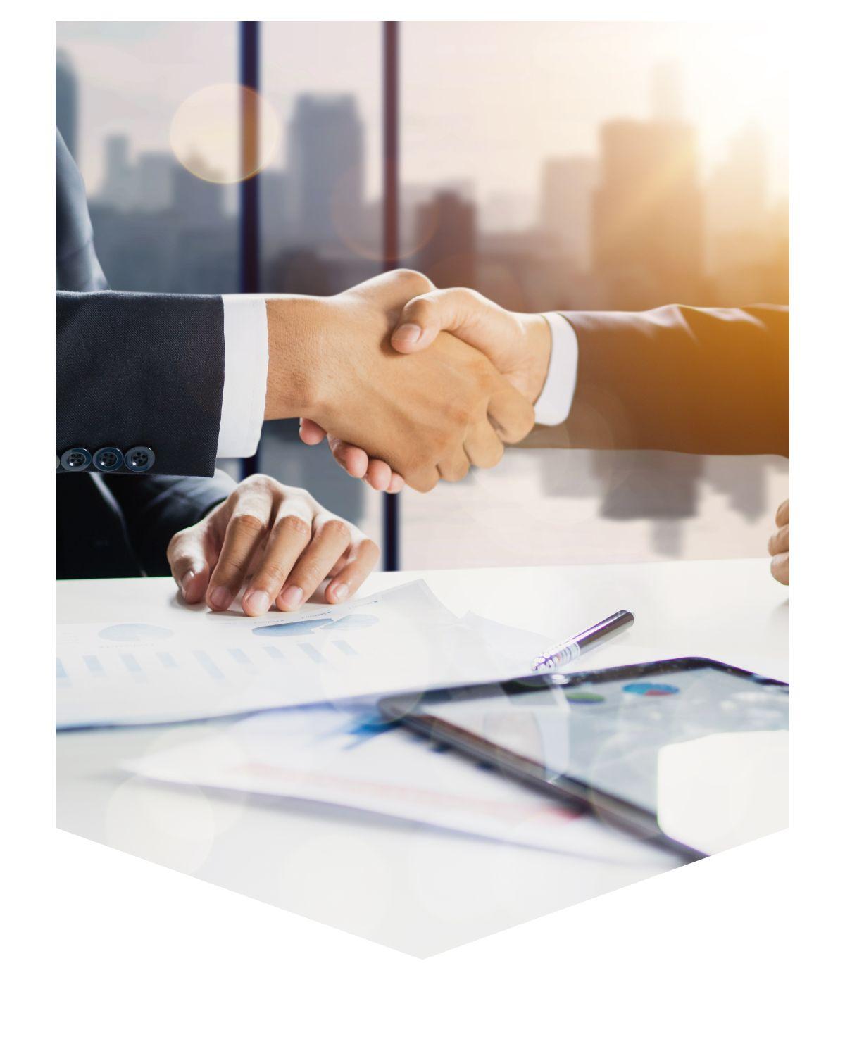 Crop of two people shaking hands at a table with paperwork under