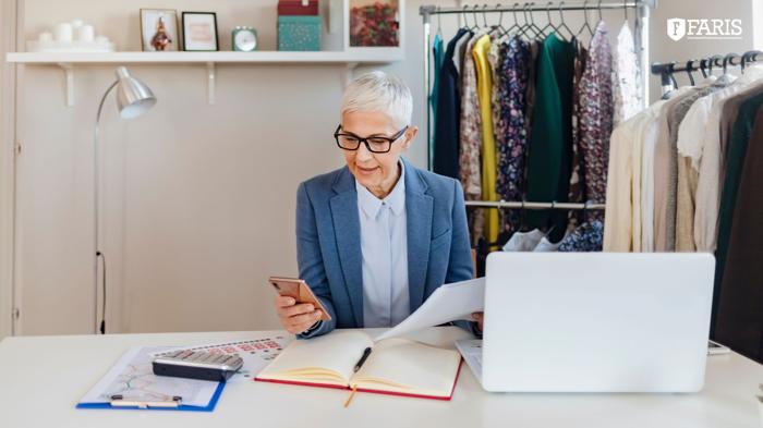 A self-employed woman reviewing documents at her retail workspace while managing taxes on her phone and laptop.