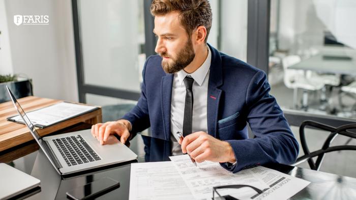 A businessman in a suit reviewing financial documents and working on tax filing at a laptop.