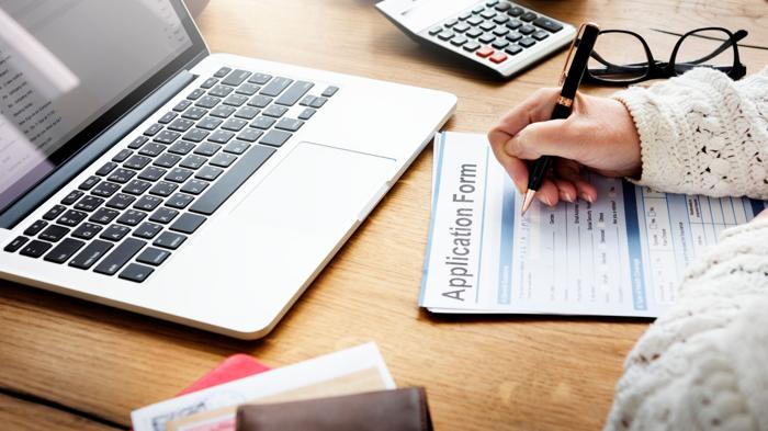 Person filling out CRA Voluntary Disclosures Program application form beside laptop, calculator, and financial documents.