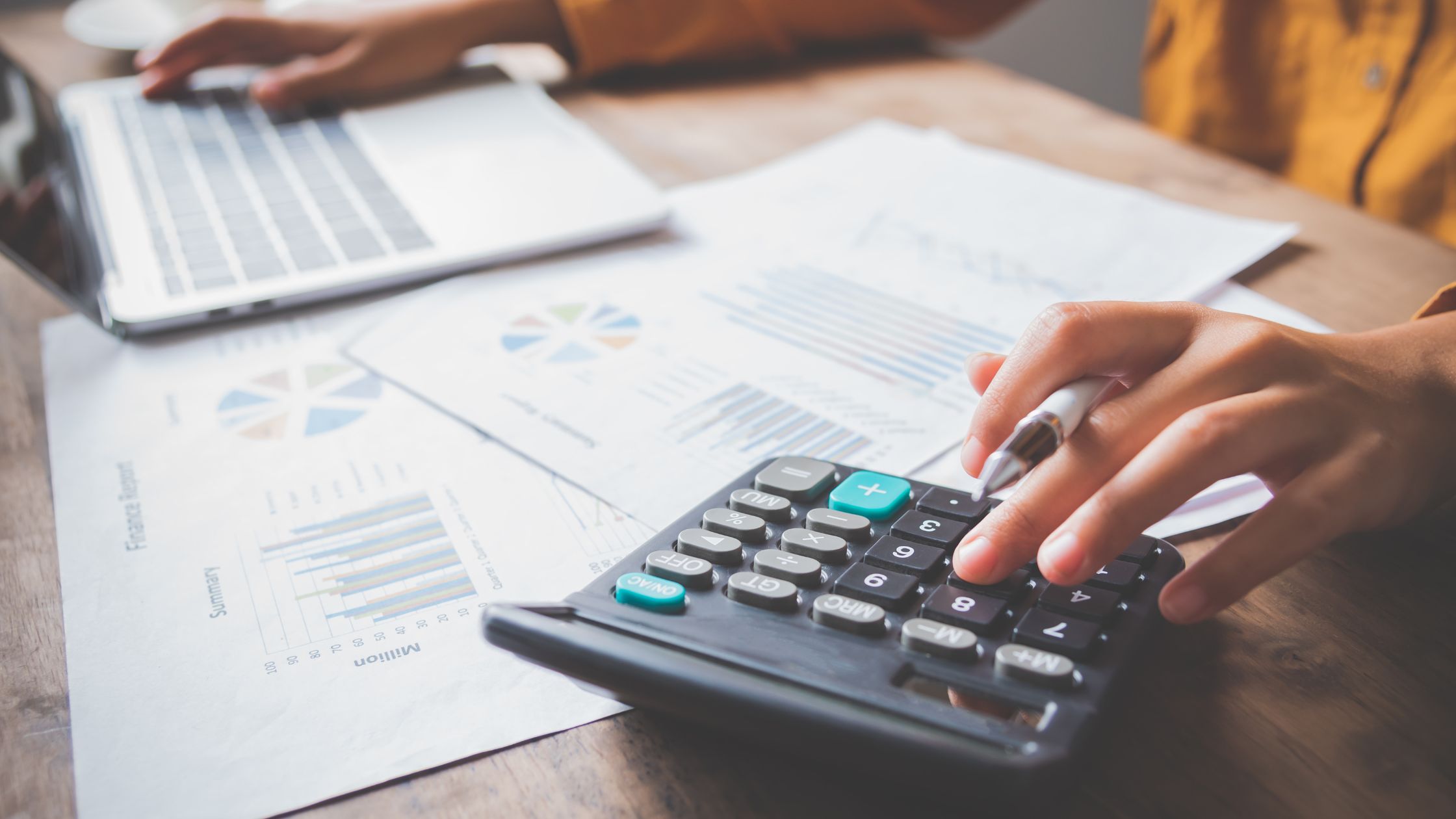 Person analyzing financial statements with a calculator and laptop, representing CRA net worth audits and income verification.