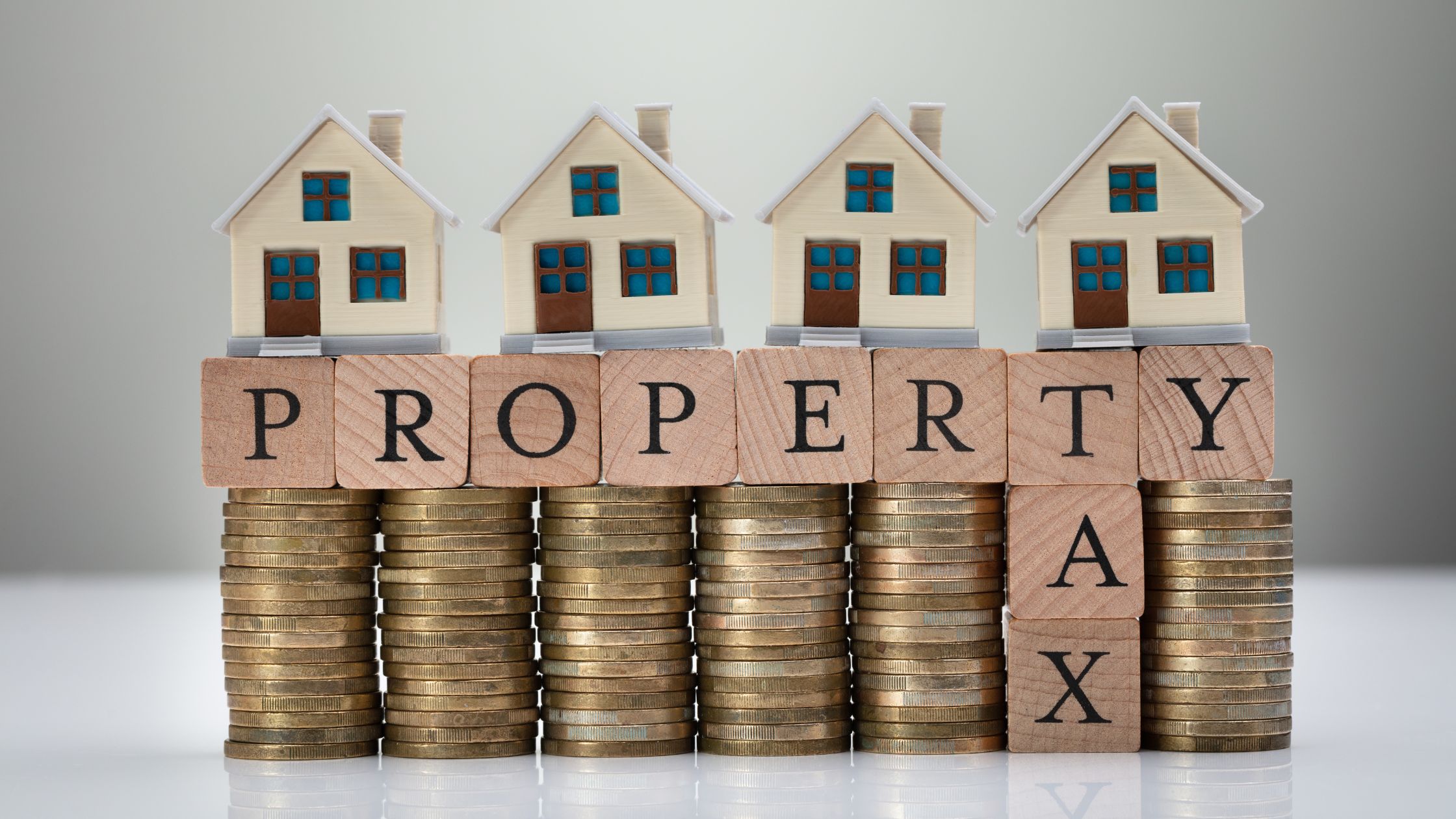 Miniature houses placed on stacks of coins spelling the word “Property Tax,” representing Canadian property and housing tax concepts.