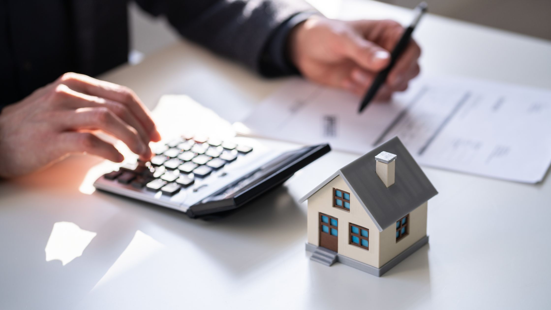 Homeowner calculating property taxes with a small house model beside paperwork, illustrating UHT filing and compliance.