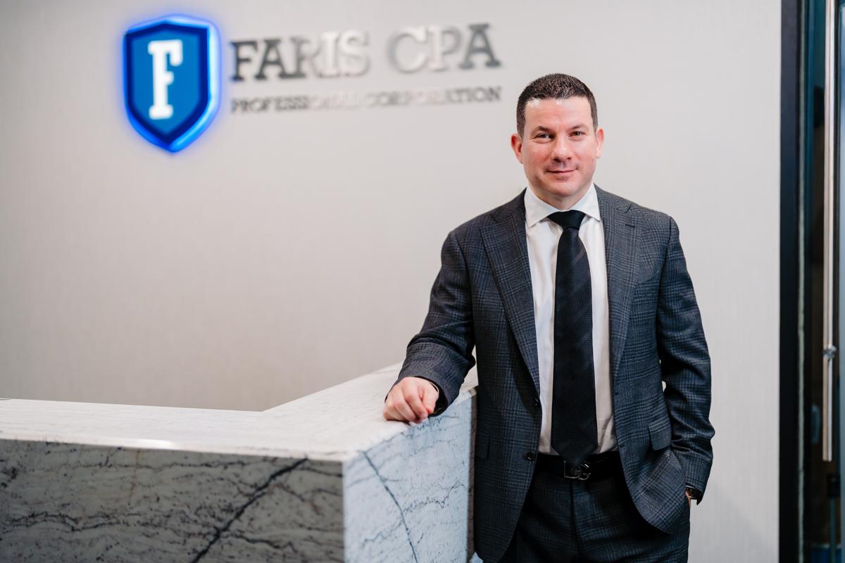 Sam standing in front of a desk with Faris CPA logo on the wall behind the desk.
