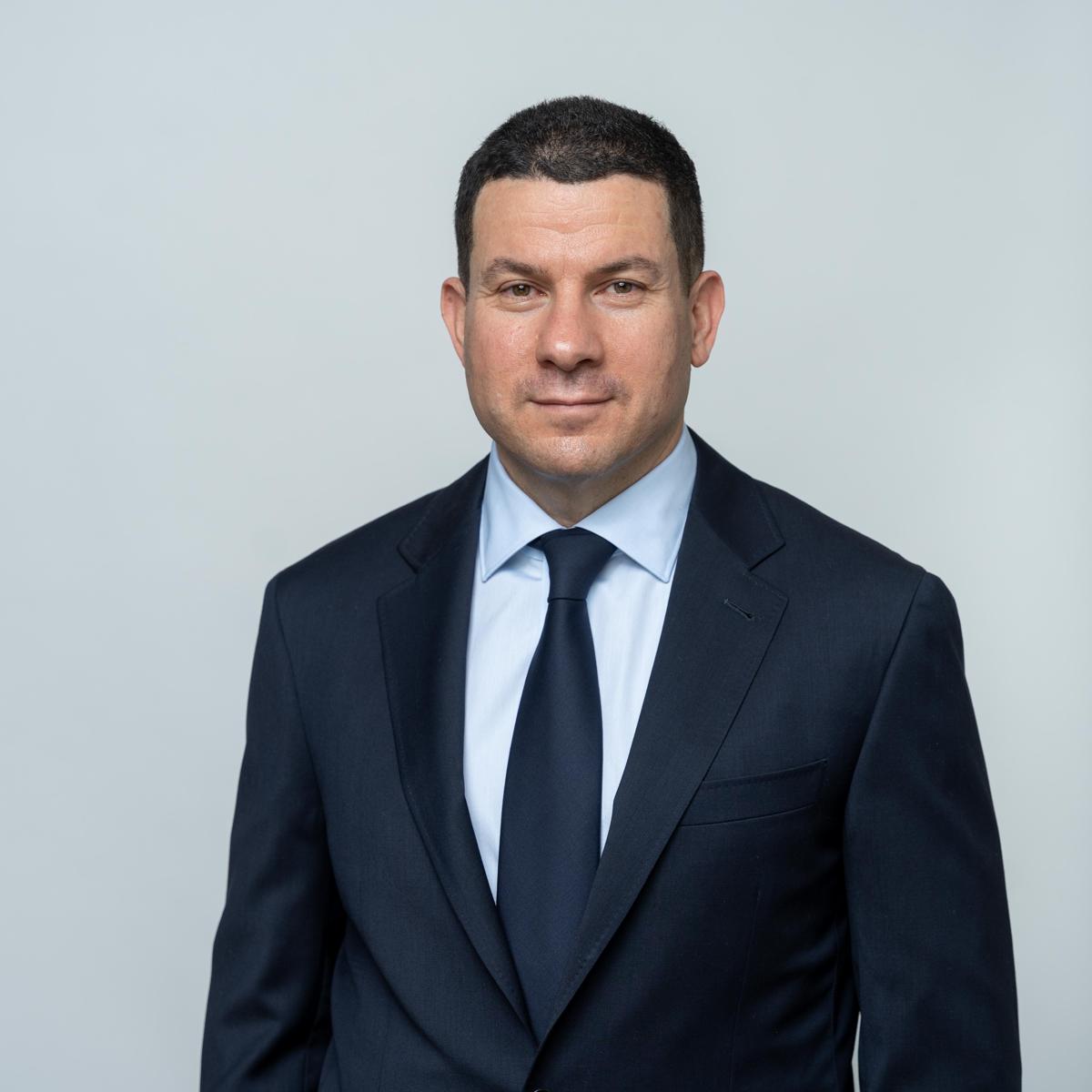 Sam wearing a blue suit smiling and looking at the camera.