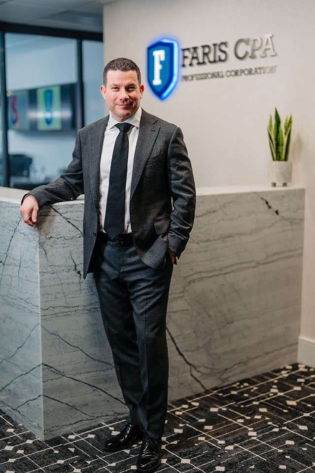 Sam Faris standing in front of desk with Faris CPA logo behind